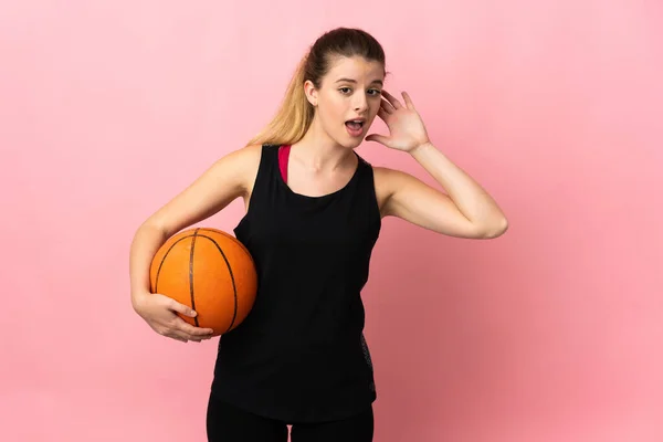 年轻的金发女子在粉色背景下打篮球 用手捂住耳朵听着什么 — 图库照片