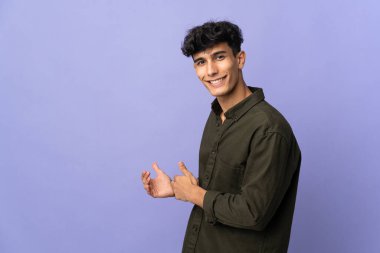 Arjantinli genç adam arka planda izole edilmiş. Davet etmek için ellerini yana uzatıyor.