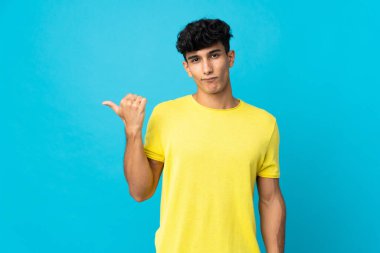 Arjantinli genç adam arka planda izole edilmiş mutsuz ve kenarı işaret ediyor.