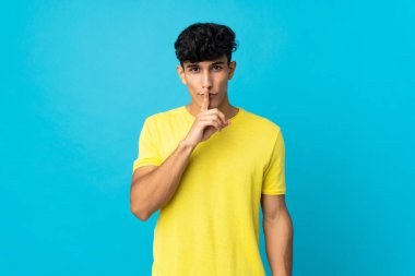 Arjantinli genç bir adam arka planda izole edilmiş. Parmağını ağzına koyduğunda sessizlik işareti gösteriyor.