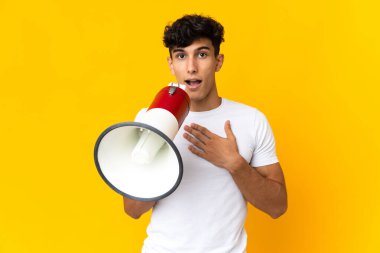 Arjantinli genç adam sarı arka planda izole edilmiş. Şaşırmış bir ifadeyle megafonla bağırıyor.