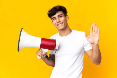 Sarı arka planda izole edilmiş genç Arjantinli bir adam elinde bir megafonla mutlu bir ifadeyle selam veriyor.