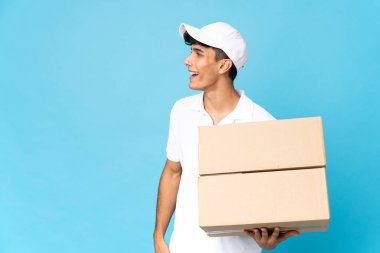 Teslimatçı Arjantinli adam mavi arka planda izole edilmiş. Yan pozisyonda gülüyor.