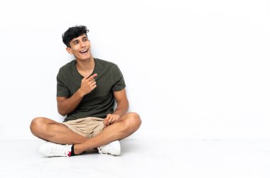 Genç Arjantinli bir adam yerde oturuyor. Parmakla göstererek bir ürün sunuyor.