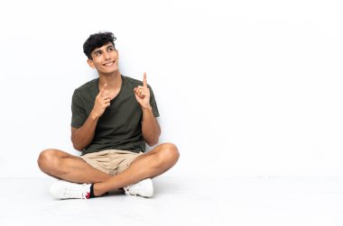 Genç Arjantinli bir adam yerde oturmuş işaret parmağıyla işaret ediyor. Harika bir fikir.