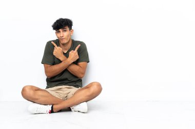 Yerde oturan genç Arjantinli adam yan taraftakileri işaret ediyor.