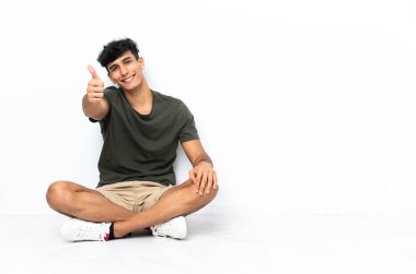 Genç Arjantinli adam, iyi bir şey olduğu için baş parmağıyla yerde oturuyor.