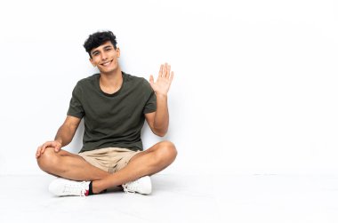 Genç Arjantinli adam yerde oturmuş mutlu bir ifadeyle selamlıyor.