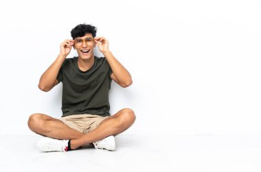 Genç Arjantinli adam gözlükleriyle yerde oturuyor ve şaşırdı.