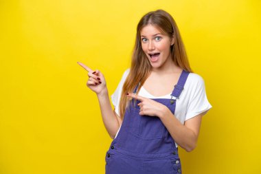 Sarı arka planda izole edilmiş genç beyaz kadın şaşırmış ve işaret ediyor.