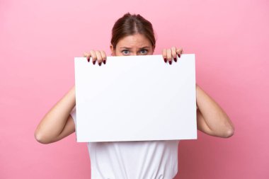 Pembe arka planda izole edilmiş beyaz bir kadın boş bir levha tutuyor ve arkasında saklanıyor.