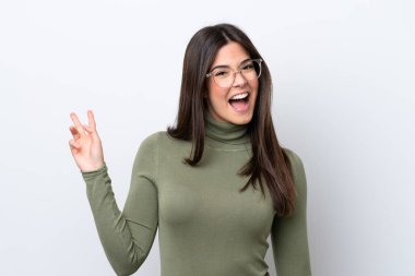 Beyaz arka planda izole edilmiş genç Brezilyalı kadın gülümsüyor ve zafer işareti gösteriyor.