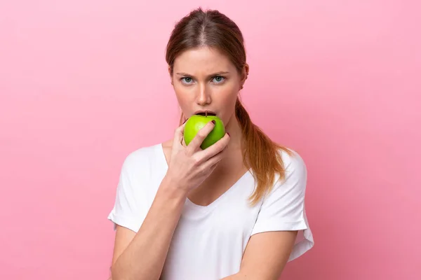 被粉色背景隔离的年轻高加索女人吃苹果 — 图库照片