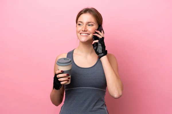 ピンクの背景に隔離された若いスポーツの白人女性取り去るためにコーヒーを保持し 携帯電話 — ストック写真