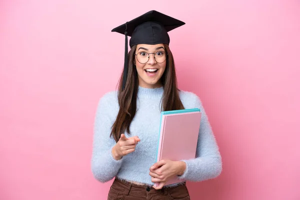 若いです学生ブラジル人女性身に着けています卒業帽子絶縁上のピンクの背景驚きと指摘フロント — ストック写真