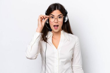 Beyaz arka planda gözlüklü ve şaşırmış bir şekilde kulaklıkla çalışan beyaz pazarlamacı kadın.