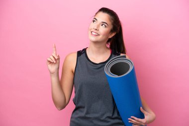 Genç Brezilyalı spor kadın yoga derslerine giderken elinde pembe arka planda izole edilmiş bir minder tutarak harika bir fikre işaret ediyor.