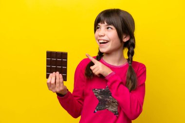 Sarı arka planda çikolata kaplı küçük beyaz kız parmağını kaldırarak çözümü bulmaya çalışıyor.