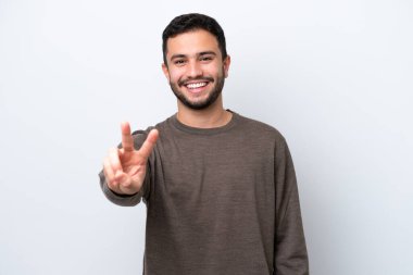 Beyaz arka planda izole edilmiş genç Brezilyalı adam gülümsüyor ve zafer işareti gösteriyor