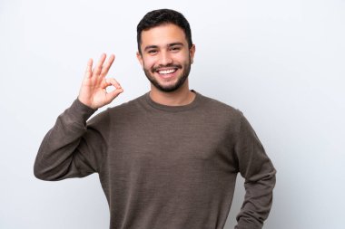 Beyaz arka planda izole edilmiş genç Brezilyalı adam parmaklarıyla tamam işareti gösteriyor