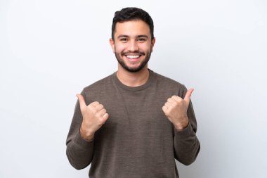 Beyaz arka planda izole edilmiş genç Brezilyalı bir adam. Baş parmakları havada ve gülümsüyor.