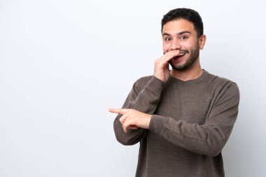 Beyaz arka planda izole edilmiş genç Brezilyalı bir adam bir ürün sunmak ve bir şeyler fısıldamak için kenarı işaret ediyor.