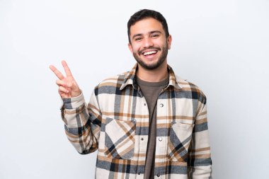 Beyaz arka planda izole edilmiş genç Brezilyalı adam gülümsüyor ve zafer işareti gösteriyor