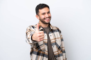 Genç Brezilyalı adam beyaz arka planda izole edildi. Başparmakları havada çünkü iyi bir şey oldu.