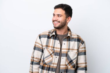 Genç Brezilyalı bir adam beyaz arka planda izole edilmiş, yana bakıyor ve gülümsüyor.