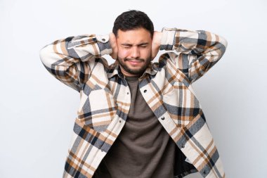 Beyaz arka planda izole edilmiş genç Brezilyalı adam hayal kırıklığına uğramış ve kulaklarını kapatmış.