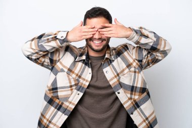 Genç Brezilyalı bir adam beyaz arka planda izole edilmiş gözleri elleriyle kaplıyor ve gülümsüyor.