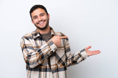 Beyaz arka planda izole edilmiş genç Brezilyalı bir adam bir ilan vermek için avucunun içinde hayali bir mekan tutuyor.