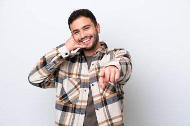 Beyaz arka planda izole edilmiş genç Brezilyalı bir adam telefon hareketi yapıyor ve ön tarafı işaret ediyor.