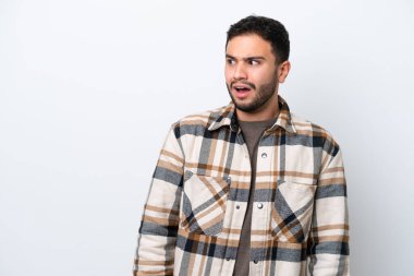 Beyaz arka planda izole edilmiş genç Brezilyalı adam yan tarafa bakarken sürpriz jest yapıyor.