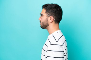 Mavi arka planda gözlüklü genç Brezilyalı adam izole edilmiş.