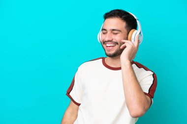Genç Brezilyalı adam mavi arka planda izole edilmiş müzik dinliyor ve şarkı söylüyor.