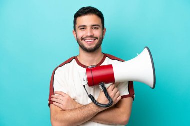 Mavi arka planda izole edilmiş genç Brezilyalı bir adam elinde bir megafon ve gülümsüyor.