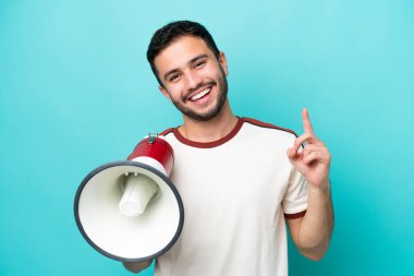 Genç Brezilyalı bir adam mavi arka planda izole edilmiş elinde bir megafonla harika bir fikre işaret ediyor.