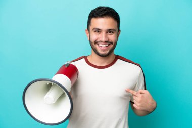 Mavi arka planda izole edilmiş genç Brezilyalı bir adam elinde bir megafonla ve şaşırtıcı bir yüz ifadesiyle
