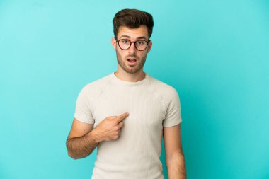 Mavi arka planda soyutlanmış beyaz tenli yakışıklı bir adam kendini işaret ediyor.