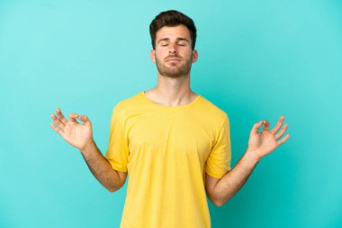 Beyaz tenli yakışıklı adam, mavi arka planda Zen pozuyla izole edilmiş.