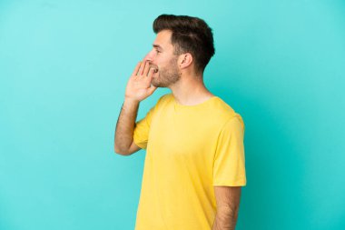 Mavi arka planda izole edilmiş, ağzı sonuna kadar açık bağıran beyaz, yakışıklı bir genç.