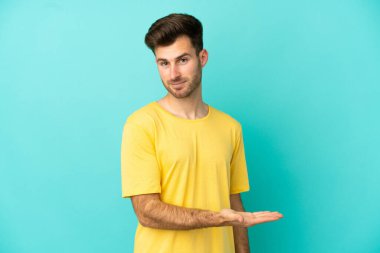 Beyaz tenli yakışıklı adam mavi arka planda izole edilmiş bir şekilde bir fikir sunuyor.