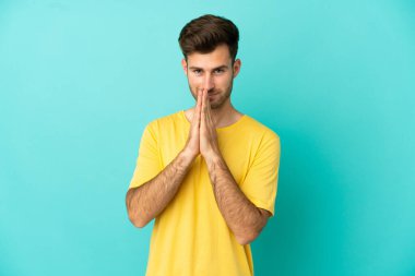 Mavi arka planda izole edilmiş beyaz tenli yakışıklı adam avuç içlerini bir arada tutuyor. İnsan bir şey ister.