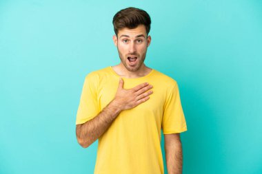 Mavi arka planda izole edilmiş beyaz, yakışıklı genç adam sağa bakarken şaşırmış ve şok olmuştu.