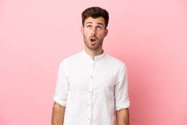 Beyaz tenli yakışıklı adam pembe arka planda izole edilmiş yukarı bakıyor ve şaşırmış bir ifadeyle