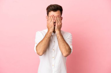 Beyaz tenli yakışıklı, pembe arka planda izole edilmiş, gözleri elle kaplanmış.