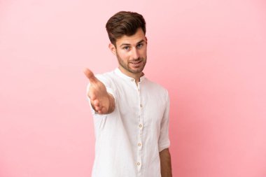 Beyaz tenli yakışıklı adam pembe arka planda izole edilmiş ve iyi bir anlaşma için el sıkışıyor.