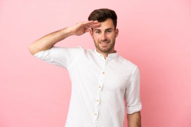 Beyaz tenli yakışıklı adam pembe arka planda izole edilmiş, mutlu bir ifadeyle selamlanıyor.