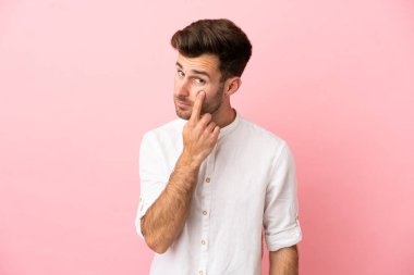 Pembe arka planda izole edilmiş beyaz yakışıklı bir adam bir şey gösteriyor.